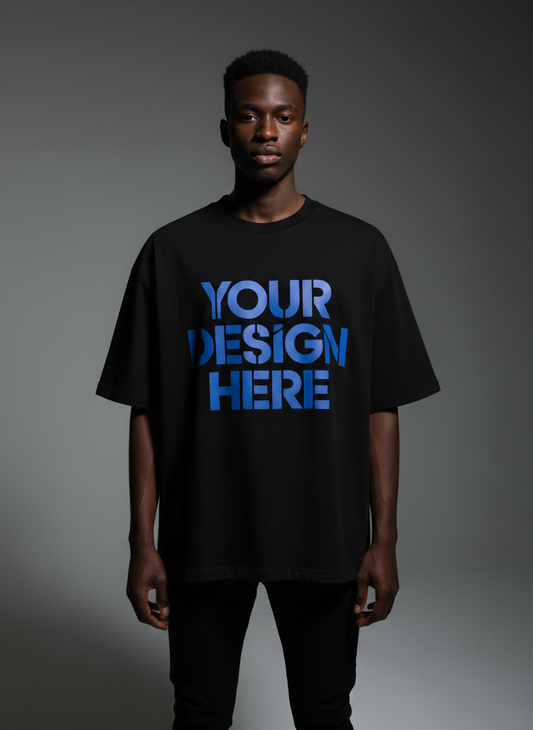 A male model in an oversized black t-shirt with blue 'YOUR DESIGN HERE' text, shot against a gray studio background.